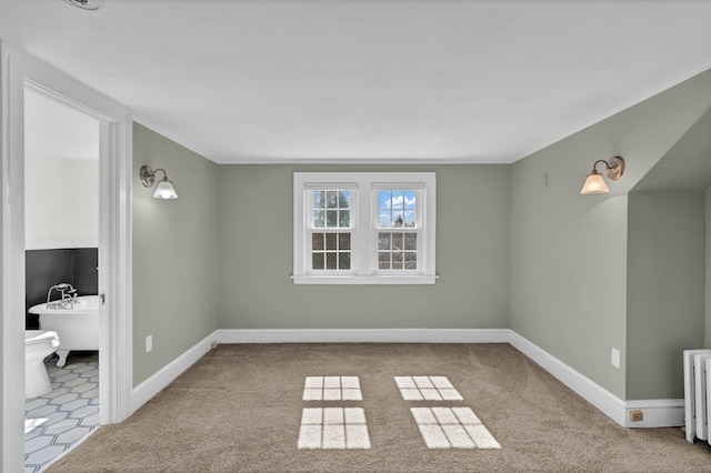 carpeted spare room featuring baseboards and radiator