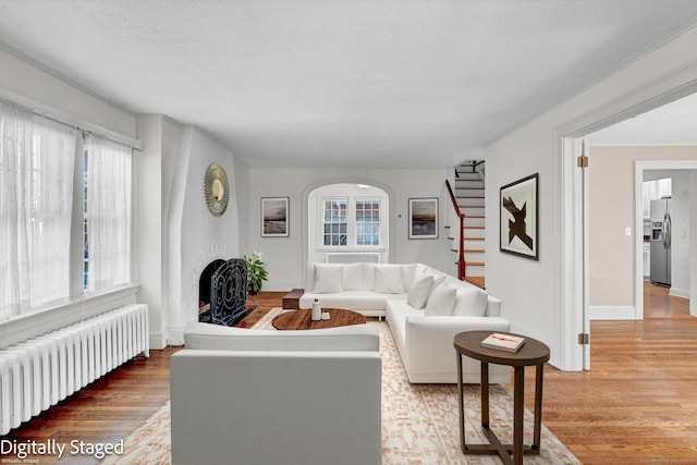 living area featuring a textured ceiling, a fireplace with raised hearth, wood finished floors, and radiator heating unit