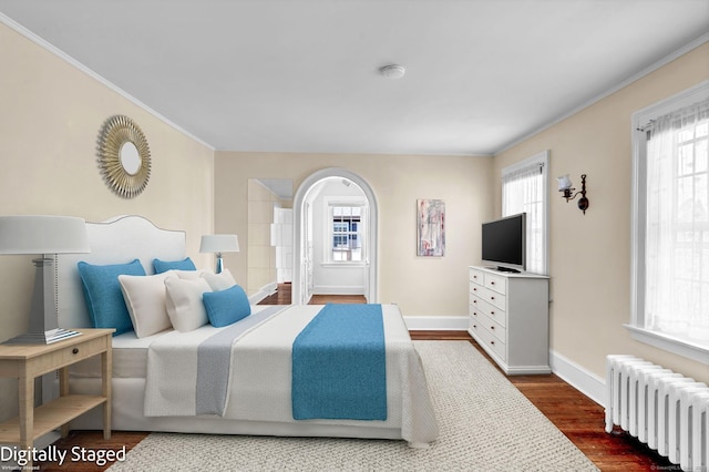 bedroom featuring dark wood-type flooring, arched walkways, radiator, crown molding, and baseboards