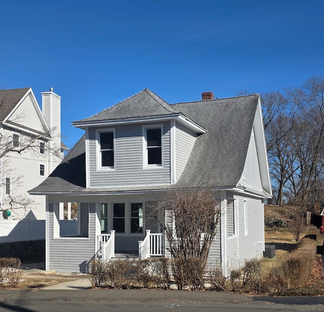 traditional-style house featuring a porch, a chimney, and a shingled roof