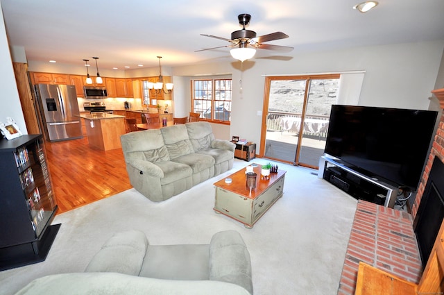 living room featuring a brick fireplace, recessed lighting, ceiling fan with notable chandelier, and light wood finished floors