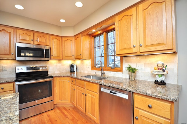 kitchen featuring a sink, stainless steel appliances, light wood finished floors, decorative backsplash, and light stone countertops