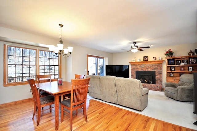 dining room with a brick fireplace, light wood-style flooring, and ceiling fan with notable chandelier