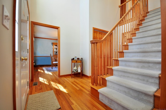 stairs with wood finished floors, visible vents, baseboards, ornamental molding, and a towering ceiling