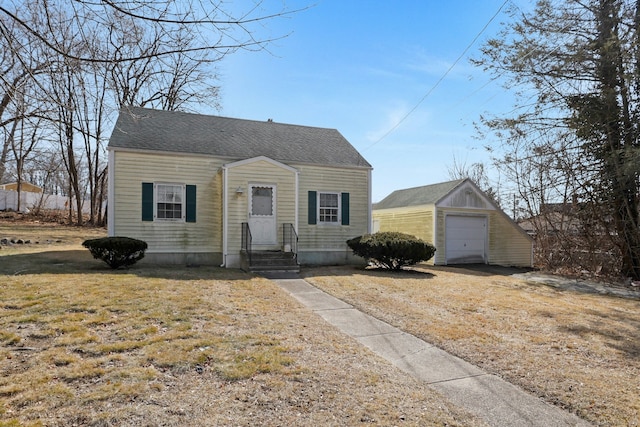 view of front of house featuring a detached garage, entry steps, a front yard, roof with shingles, and an outdoor structure