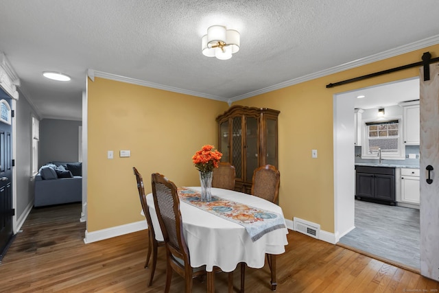 dining room featuring light wood finished floors, visible vents, a barn door, ornamental molding, and a textured ceiling