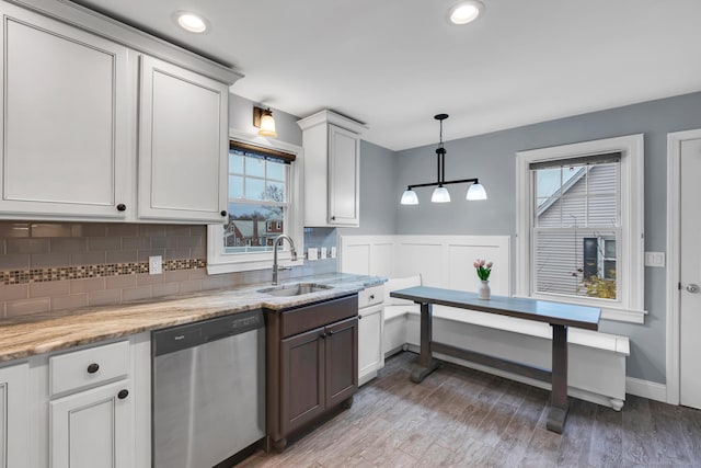 kitchen with light wood finished floors, tasteful backsplash, light stone countertops, dishwasher, and a sink