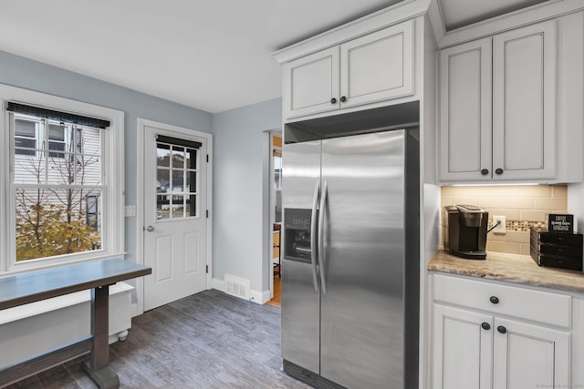 kitchen featuring visible vents, backsplash, wood finished floors, stainless steel fridge, and baseboards