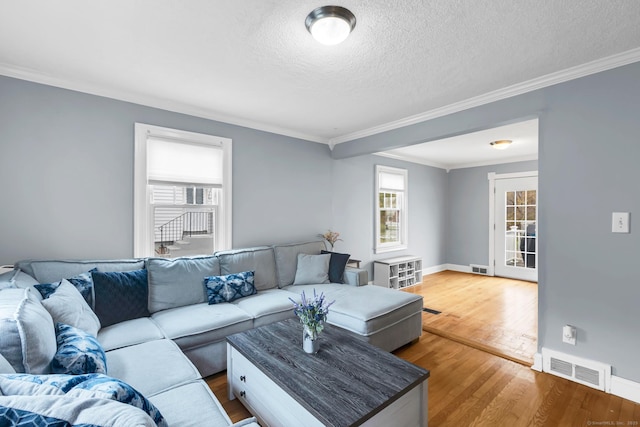 living room with visible vents, baseboards, ornamental molding, wood finished floors, and a textured ceiling