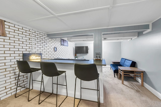 kitchen featuring dark countertops, brick wall, baseboards, a kitchen bar, and carpet floors