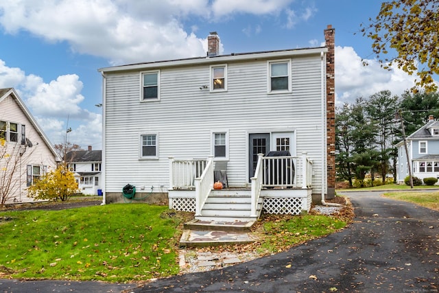 rear view of property featuring a deck, a lawn, and a chimney