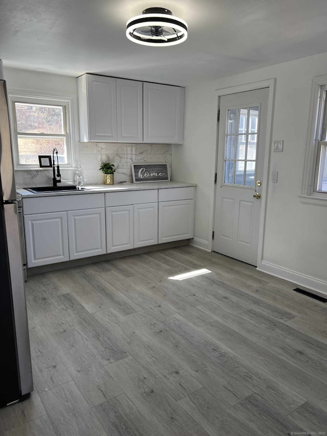 kitchen featuring white cabinetry, decorative backsplash, visible vents, and a sink