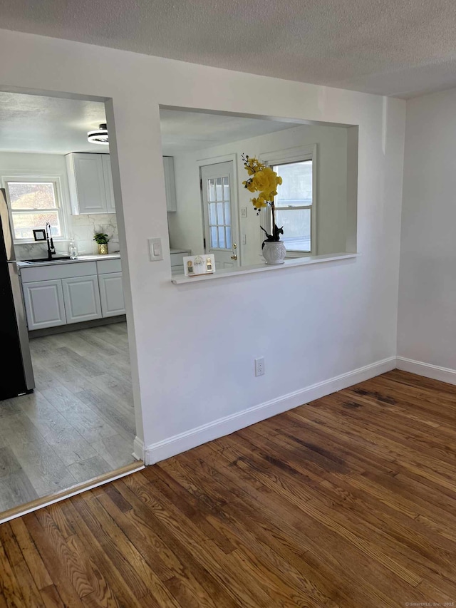 unfurnished room with a sink, a textured ceiling, baseboards, and wood finished floors