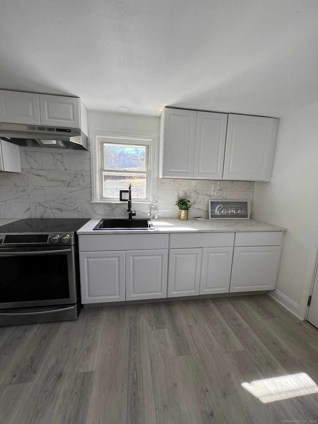 kitchen with a sink, stainless steel electric stove, under cabinet range hood, and white cabinets