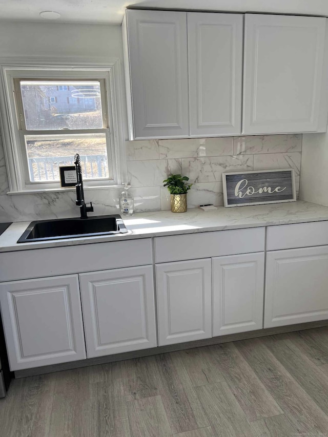 kitchen with backsplash, light wood-type flooring, light countertops, white cabinetry, and a sink