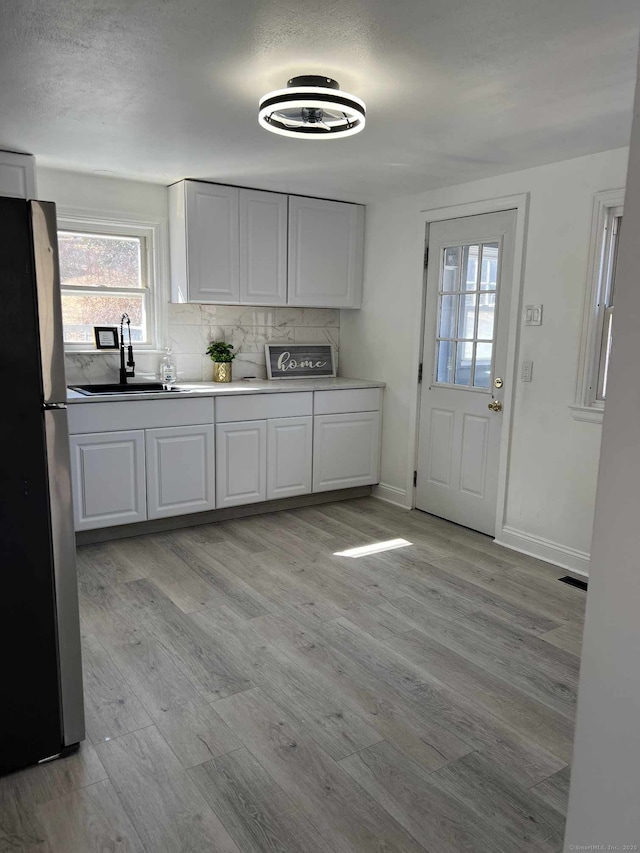 kitchen featuring tasteful backsplash, freestanding refrigerator, light wood-style floors, white cabinets, and a sink