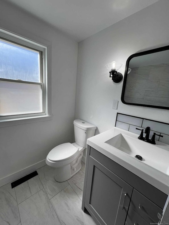 half bathroom with visible vents, toilet, marble finish floor, baseboards, and vanity