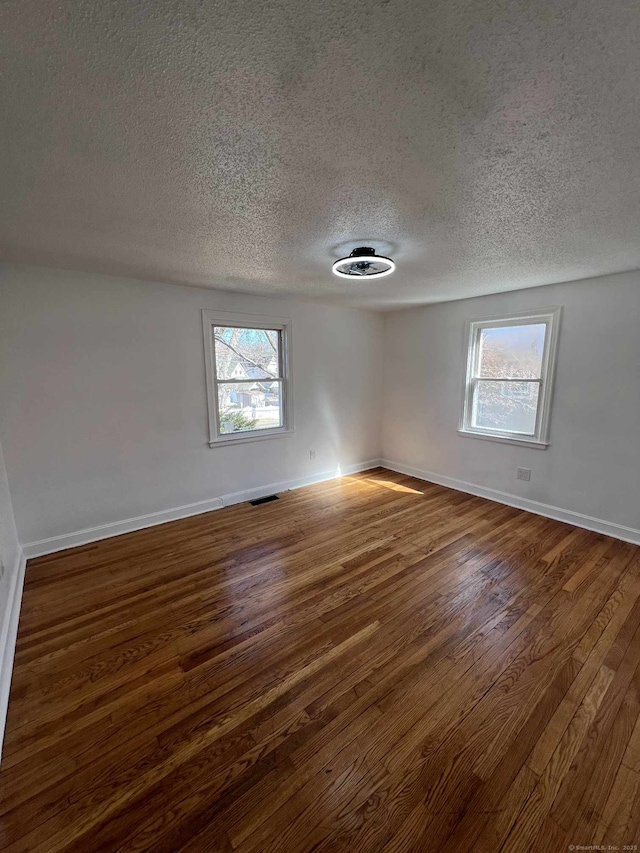 spare room with visible vents, plenty of natural light, baseboards, and dark wood finished floors