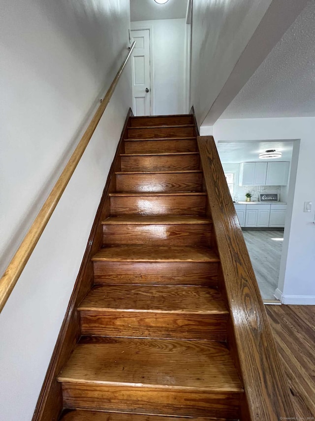 staircase with a textured ceiling and wood finished floors