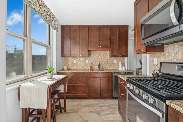 kitchen featuring a sink, light stone counters, backsplash, and appliances with stainless steel finishes