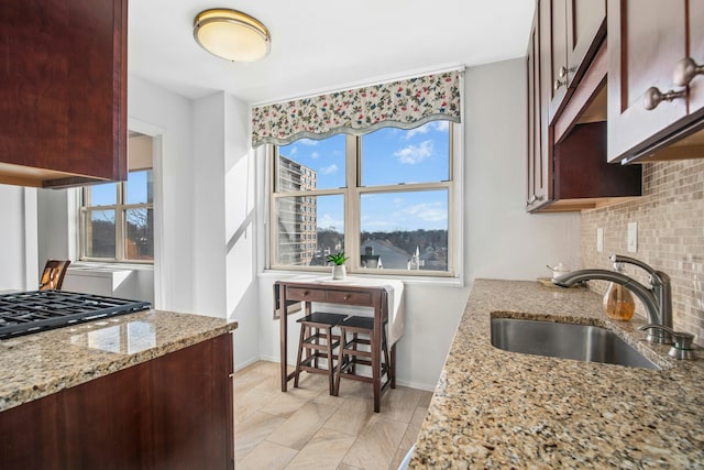 kitchen featuring baseboards, light stone countertops, stovetop, decorative backsplash, and a sink