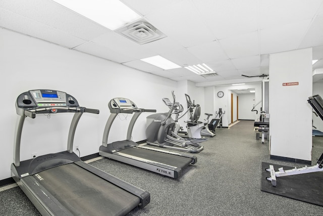 exercise room featuring visible vents, a paneled ceiling, and baseboards