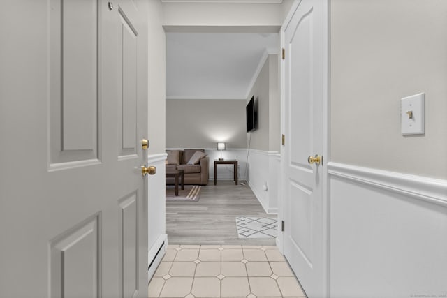 corridor featuring baseboard heating, wainscoting, and crown molding