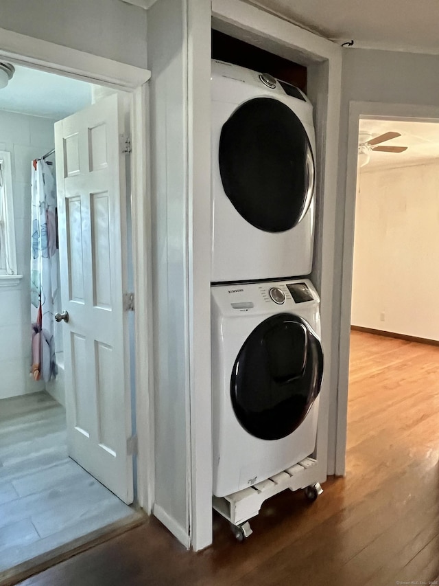 clothes washing area featuring laundry area, wood finished floors, and stacked washing maching and dryer