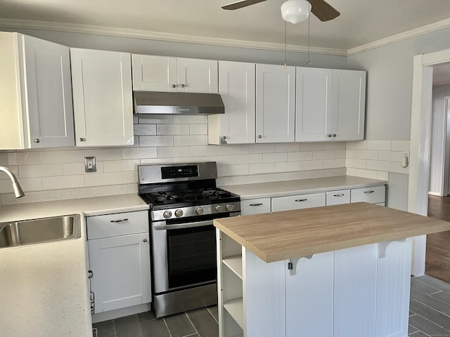 kitchen with wooden counters, a sink, under cabinet range hood, stainless steel gas range oven, and tasteful backsplash