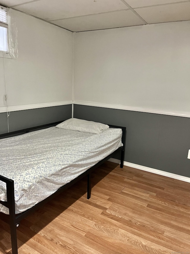 bedroom featuring wood finished floors, baseboards, and a drop ceiling