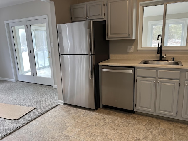 kitchen featuring a sink, stainless steel appliances, baseboards, and light countertops