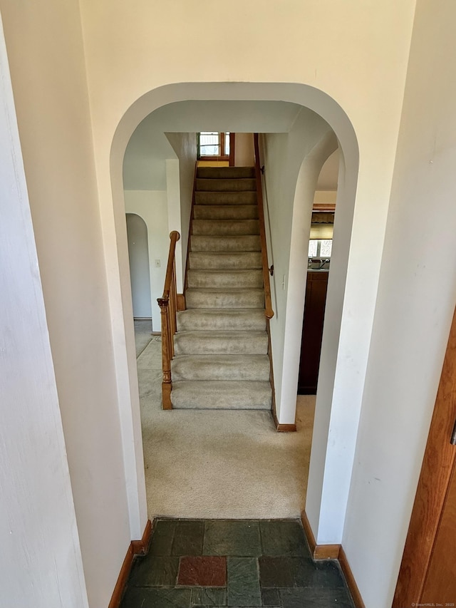 stairs featuring baseboards, arched walkways, carpet, and stone tile flooring