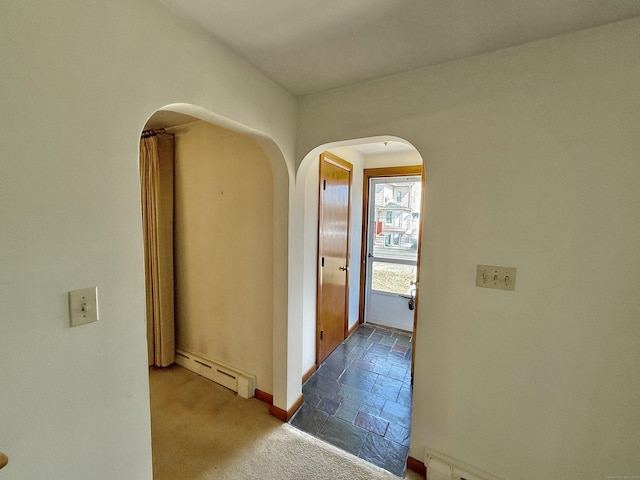 hallway featuring baseboards, arched walkways, stone tile flooring, carpet flooring, and baseboard heating