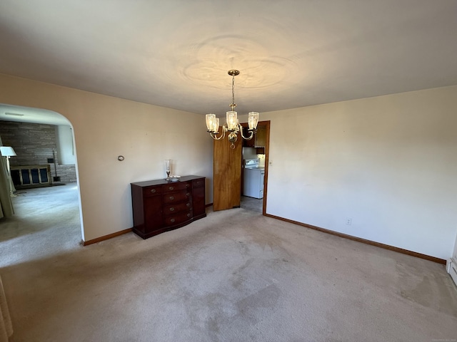 unfurnished dining area featuring light colored carpet, a notable chandelier, baseboards, and arched walkways