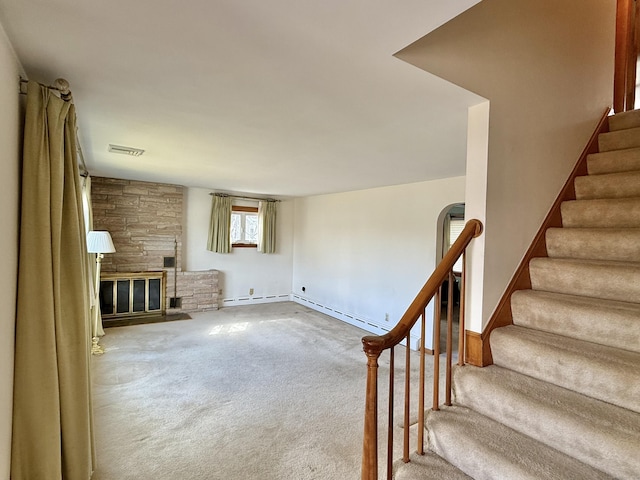 unfurnished living room featuring visible vents, carpet floors, a fireplace, stairs, and a baseboard heating unit