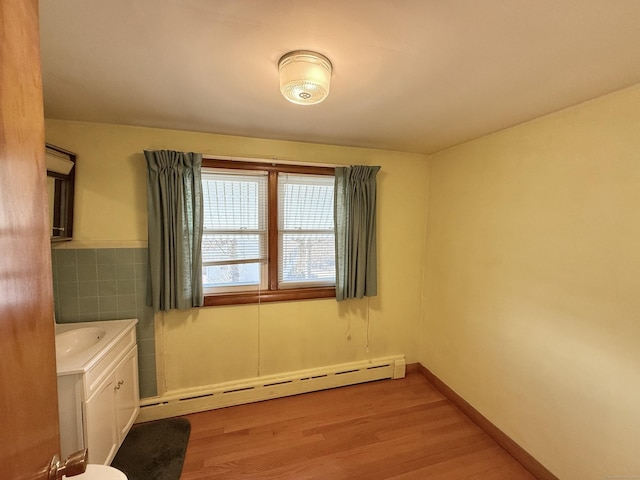 interior space with light wood-type flooring, a baseboard radiator, baseboards, and tile walls