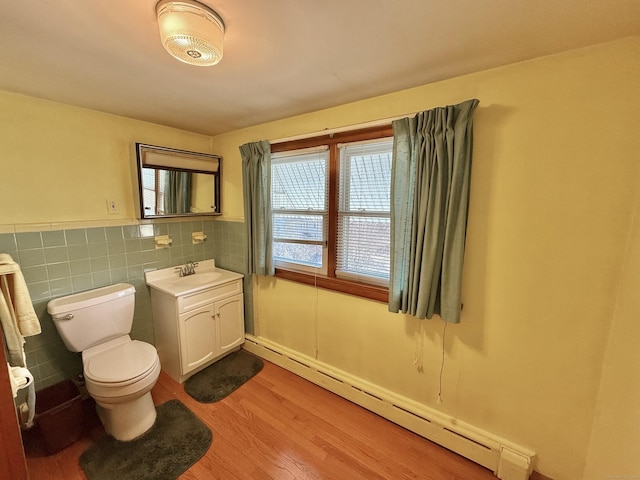 bathroom featuring toilet, wood finished floors, tile walls, baseboard heating, and vanity