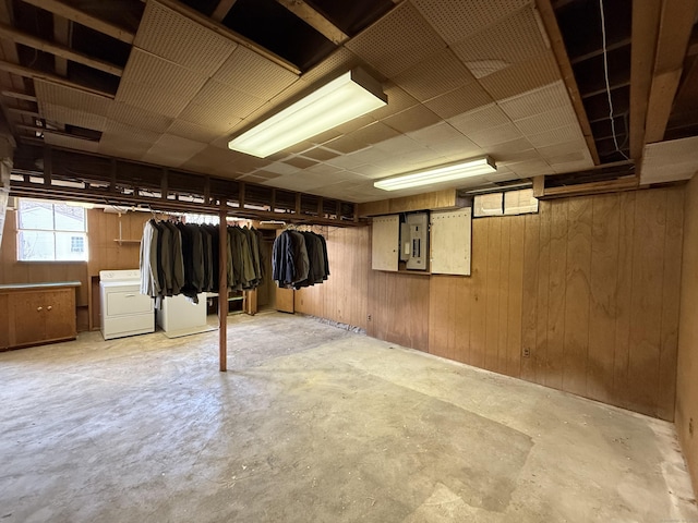 basement with wooden walls, electric panel, and washing machine and clothes dryer