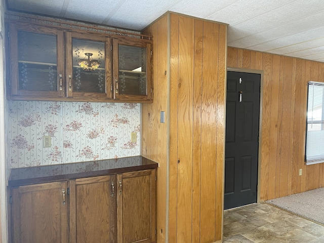 kitchen with glass insert cabinets, dark countertops, wood walls, and brown cabinetry