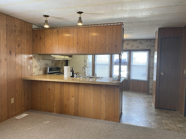 kitchen featuring under cabinet range hood, visible vents, brown cabinets, and range with gas cooktop