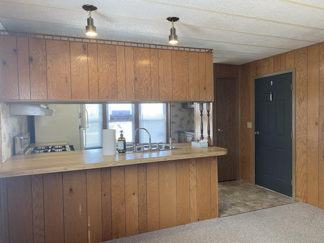 kitchen with brown cabinets, a peninsula, wood walls, and a sink