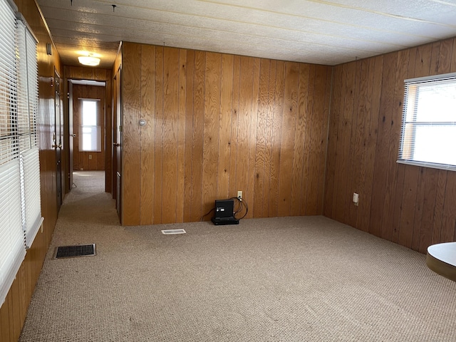 carpeted empty room featuring visible vents and wood walls