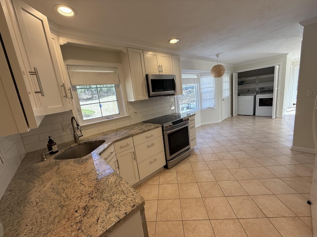 kitchen with light stone countertops, washer and clothes dryer, light tile patterned flooring, stainless steel appliances, and a sink