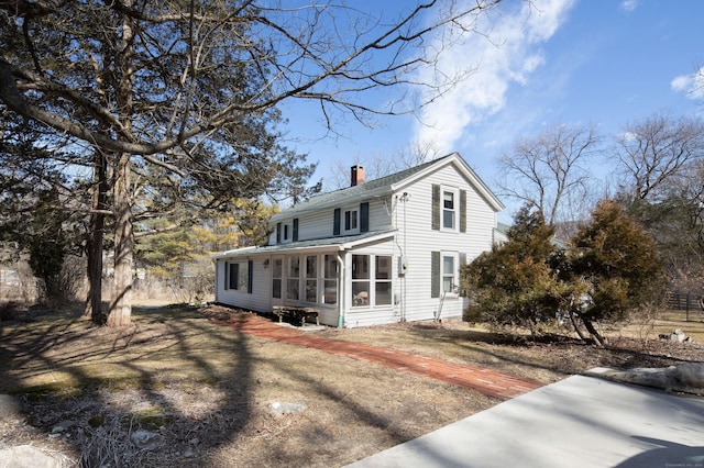 view of front facade featuring driveway, a chimney, and a sunroom