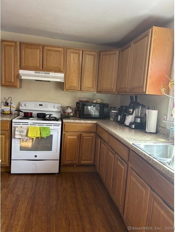 kitchen featuring under cabinet range hood, dark wood finished floors, white electric stove, brown cabinetry, and black microwave