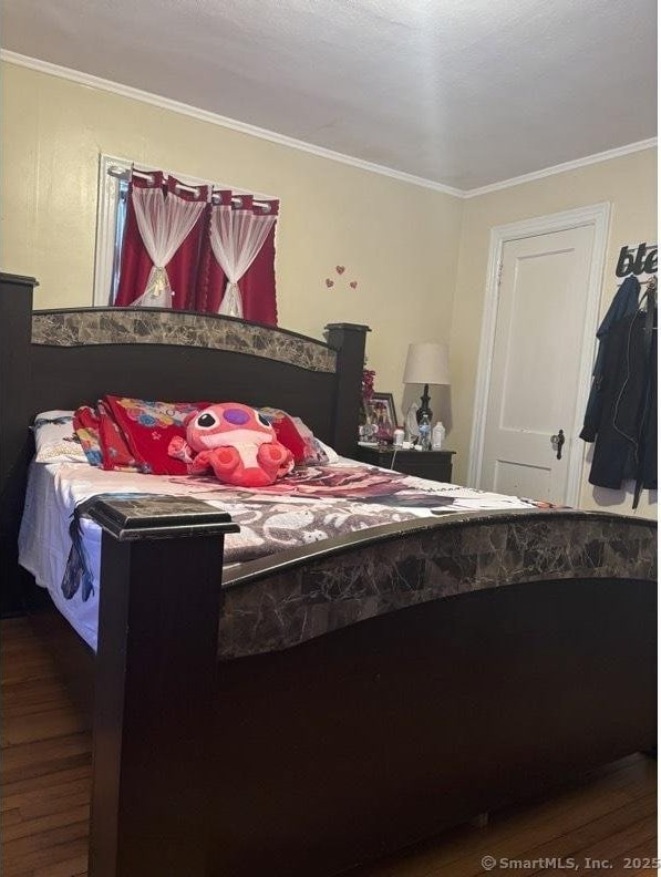 bedroom with wood finished floors and ornamental molding