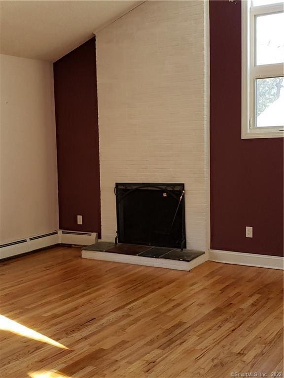 unfurnished living room with light wood finished floors, baseboard heating, a fireplace, and baseboards