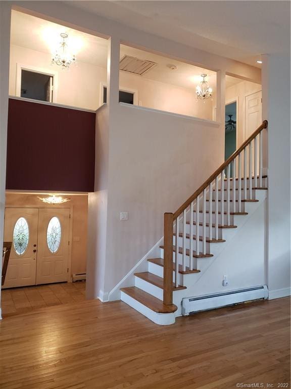 stairway with a chandelier, baseboard heating, a towering ceiling, and wood finished floors