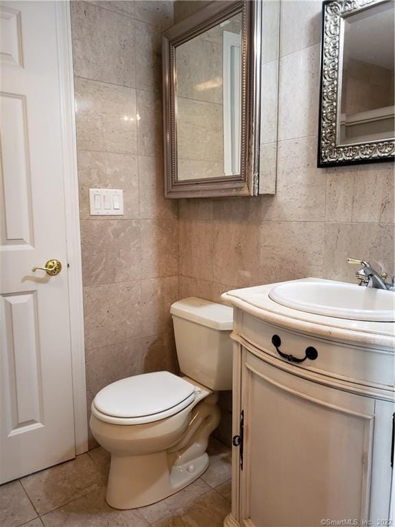 half bath featuring toilet, tile walls, tile patterned flooring, decorative backsplash, and vanity