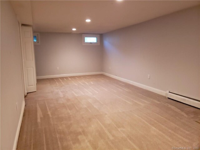 basement featuring a baseboard heating unit, recessed lighting, light colored carpet, and baseboards